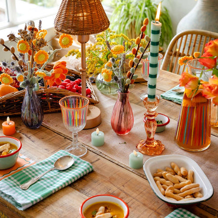 Decorative table setting with colorful candles, flowers, and food on a wooden table.