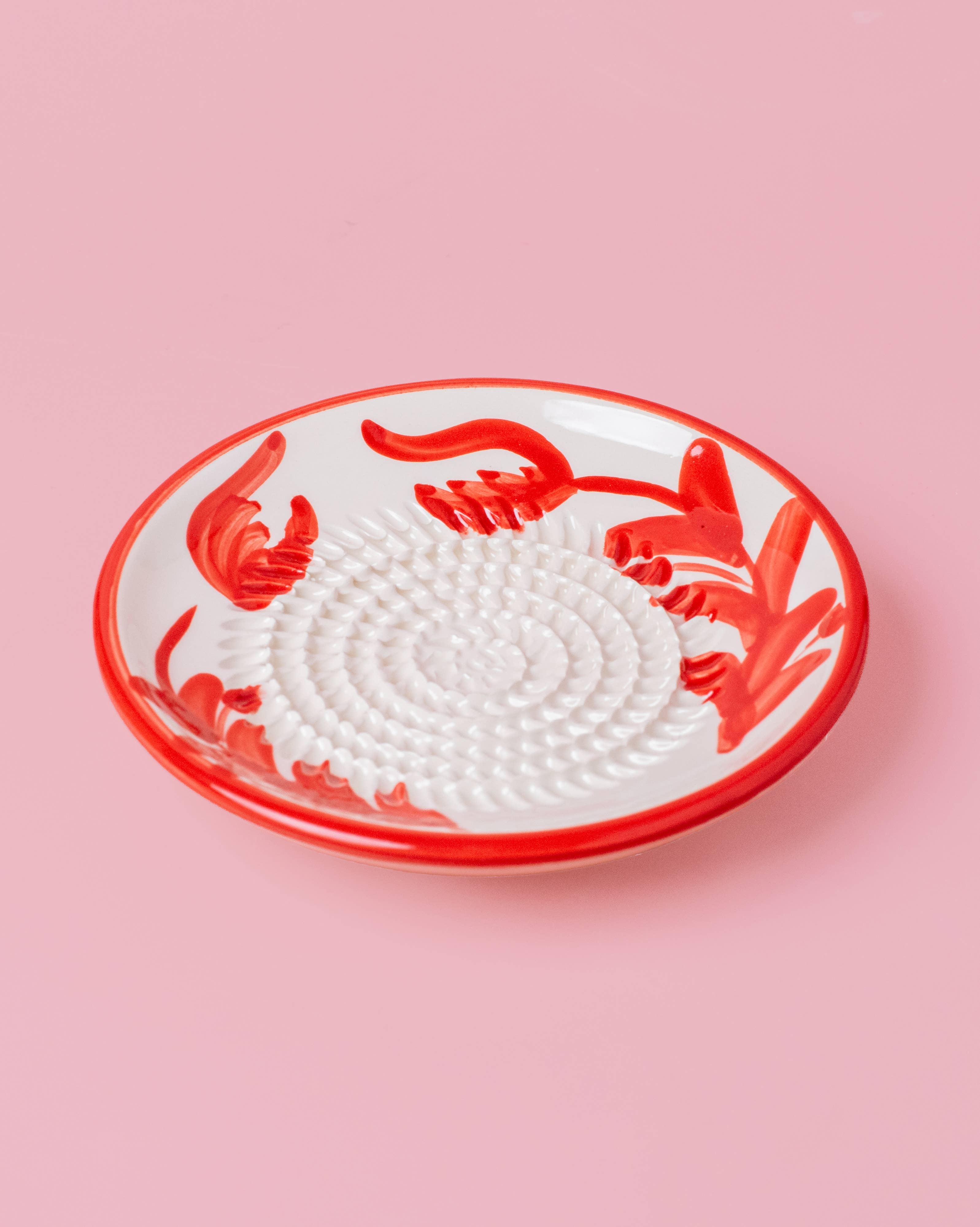 Decorative grater plate with red floral design on a pink background