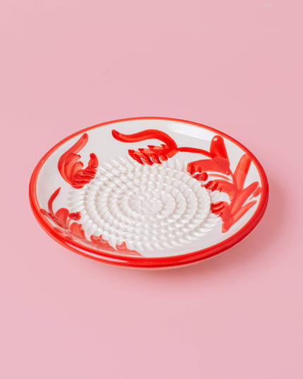 Decorative grater plate with red floral design on a pink background