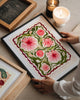 Framed floral artwork on a table with candles and a chalkboard in the background