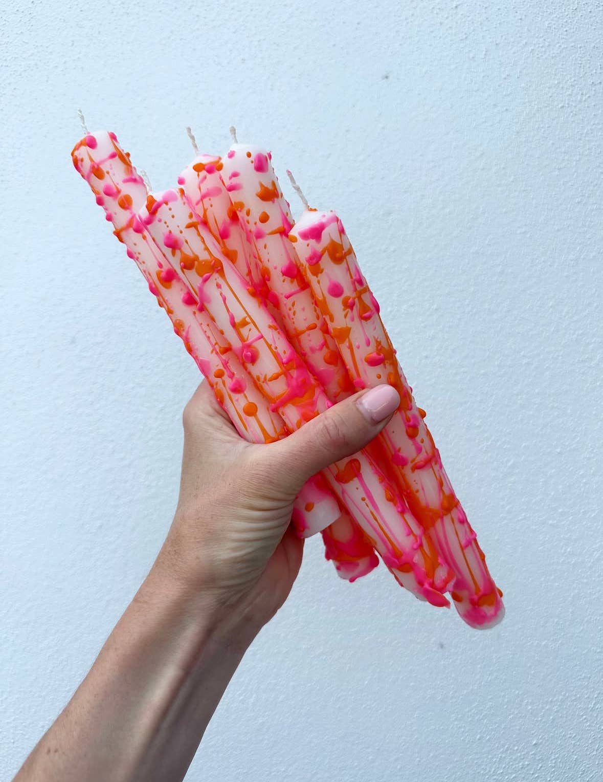 Hand holding pink and orange patterned candles against a light blue background