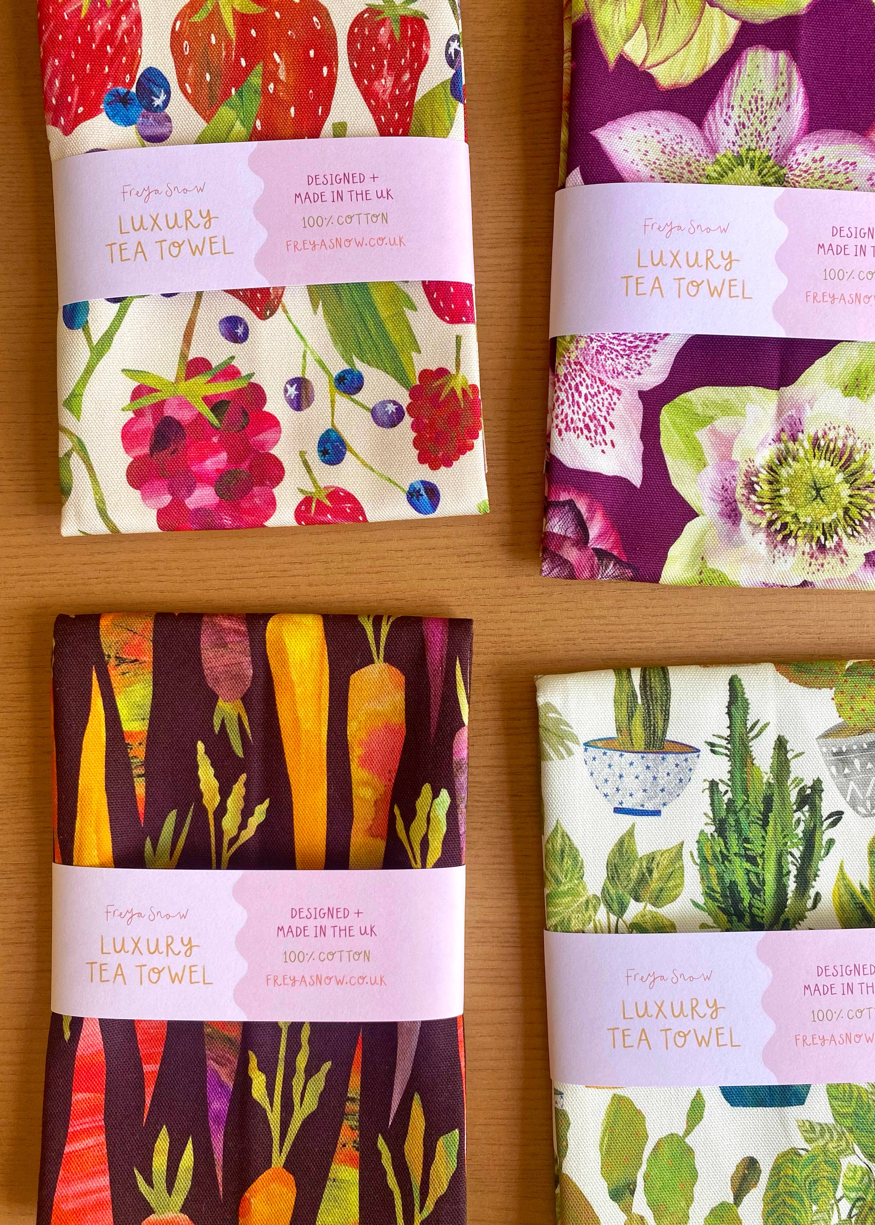 Set of four colorful tea towels with different patterns on a wooden surface.