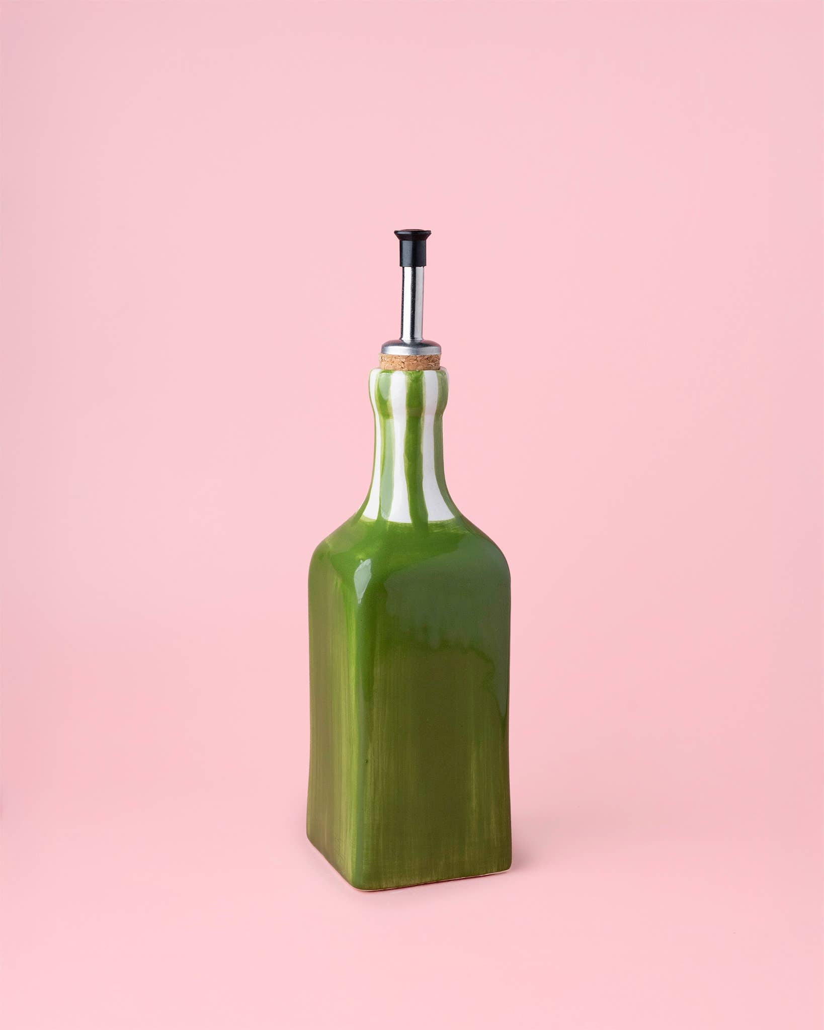 Green ceramic oil bottle with cork stopper on a pink background