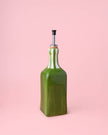 Green ceramic oil bottle with cork stopper on a pink background