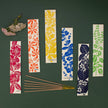 Set of colourful incense packets with floral and leaf patterns on a dark green background.