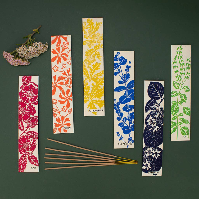 Set of colourful incense packets with floral and leaf patterns on a dark green background.