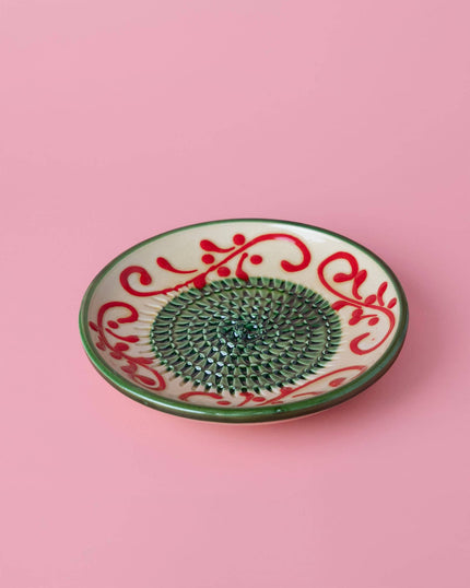 Decorative grater plate with red and green patterns on a pink background