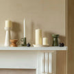 Decorative candles and holders on a white surface against a beige wall