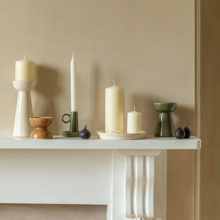 Decorative candles and holders on a white surface against a beige wall