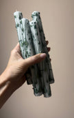 Hand holding a bundle of green candles against a beige background