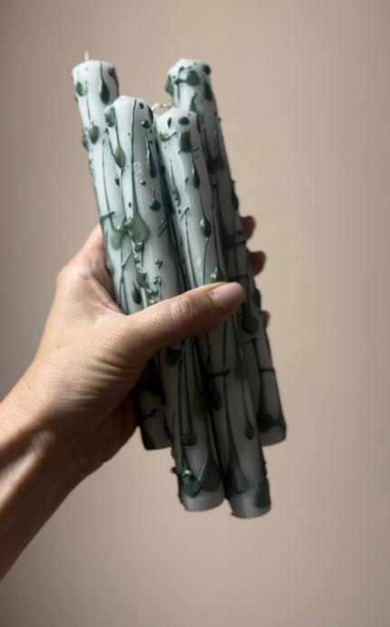 Hand holding a bundle of green candles against a beige background