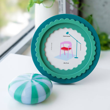 Round green frame with a small illustration on a white surface, next to a striped green and white object.