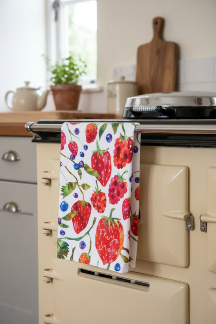Colourful pattern of strawberries, raspberries, and blueberries on a tea towel hanging on an oven.