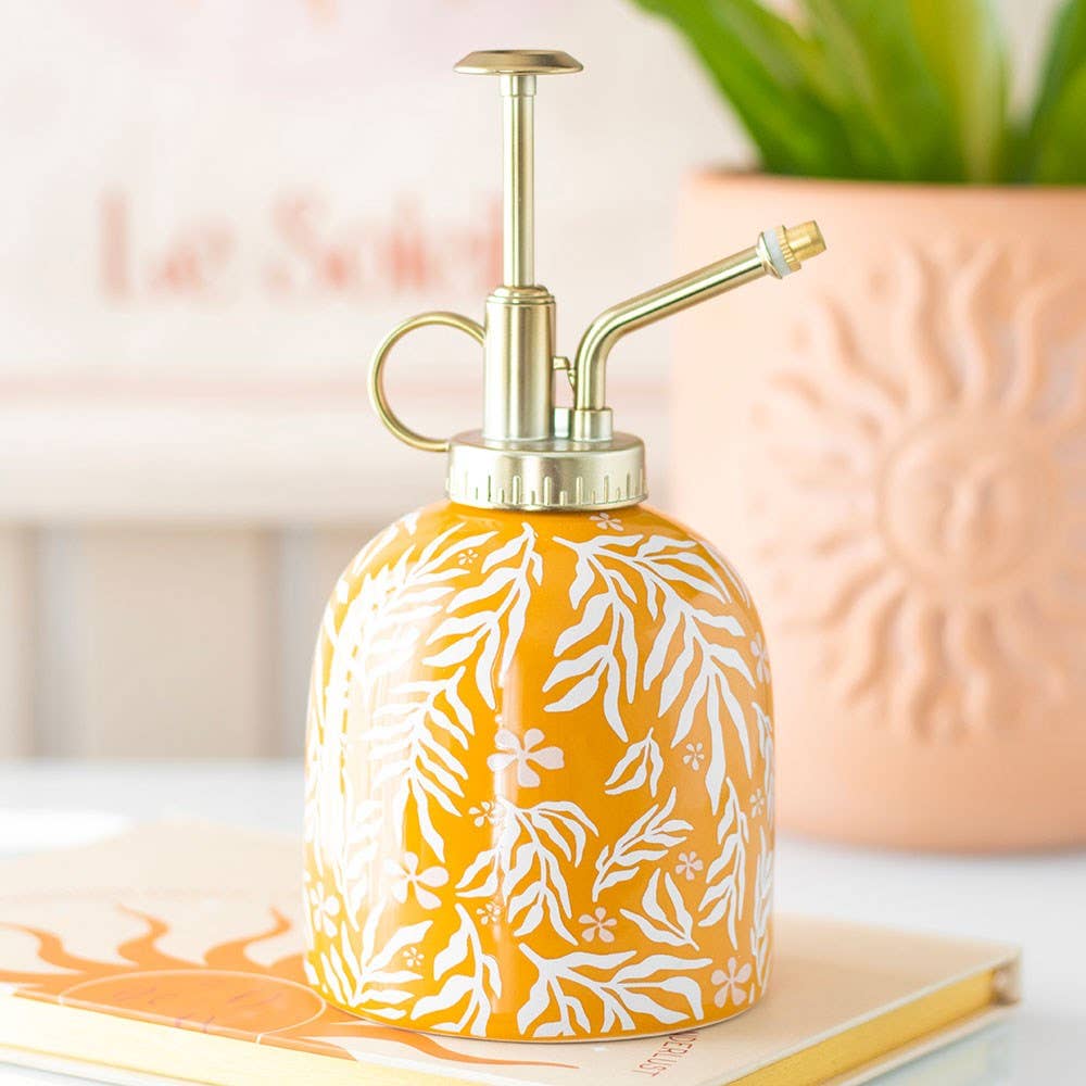 Yellow ceramic spray bottle with white leaf pattern on a surface