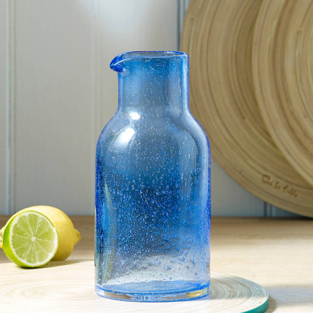 Blue glass carafe on a wooden surface with a lemon and lime