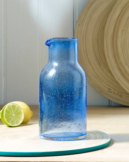 Blue glass carafe on a wooden surface with a lemon and lime