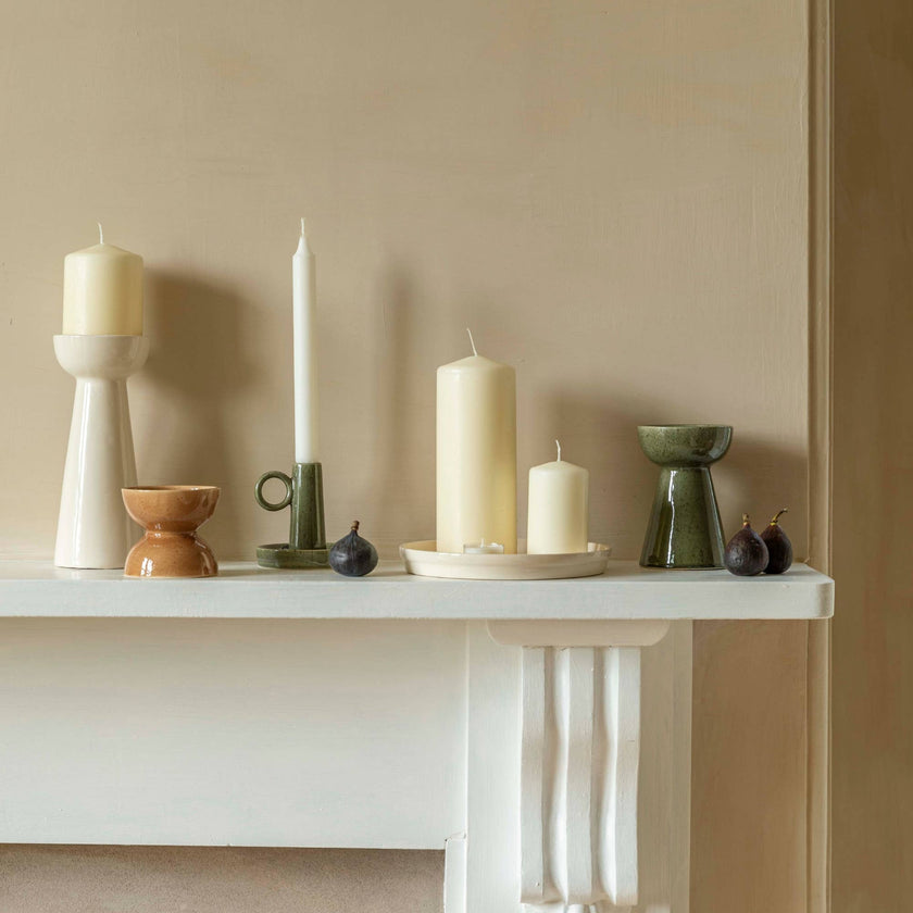Decorative candles and holders on a white surface against a beige wall