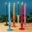 Colorful candles in glass candlesticks on a wooden surface with a blue background