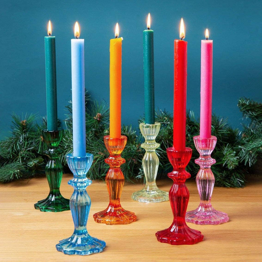 Colorful candles in glass candlesticks on a wooden surface with a blue background