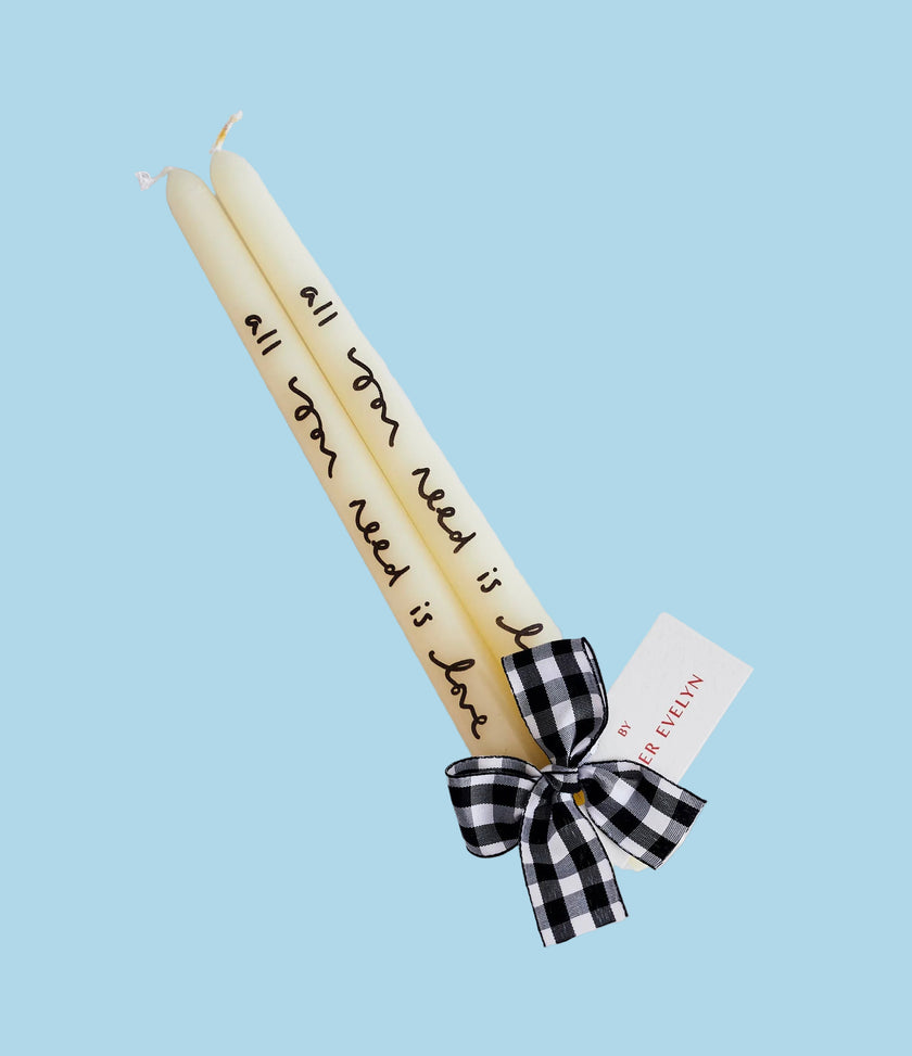 Two white candles with 'all you need is love' text and a black and white gingham bow