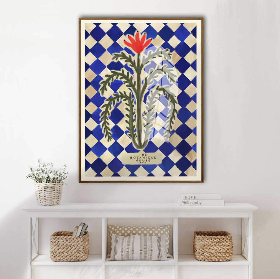 Framed artwork with a floral design on a blue and white checkered background, displayed on a wall above a white shelf.