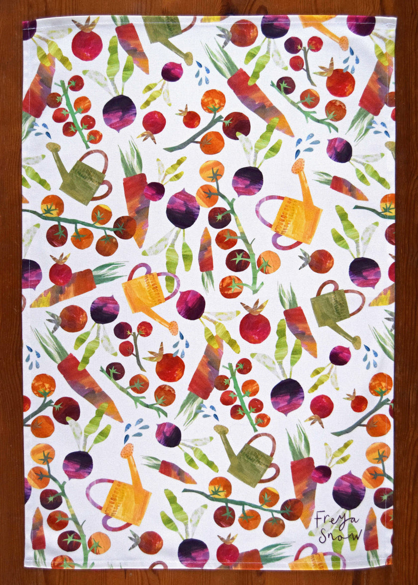 Colorful garden-themed tea towel with vegetables and watering cans on a white background.