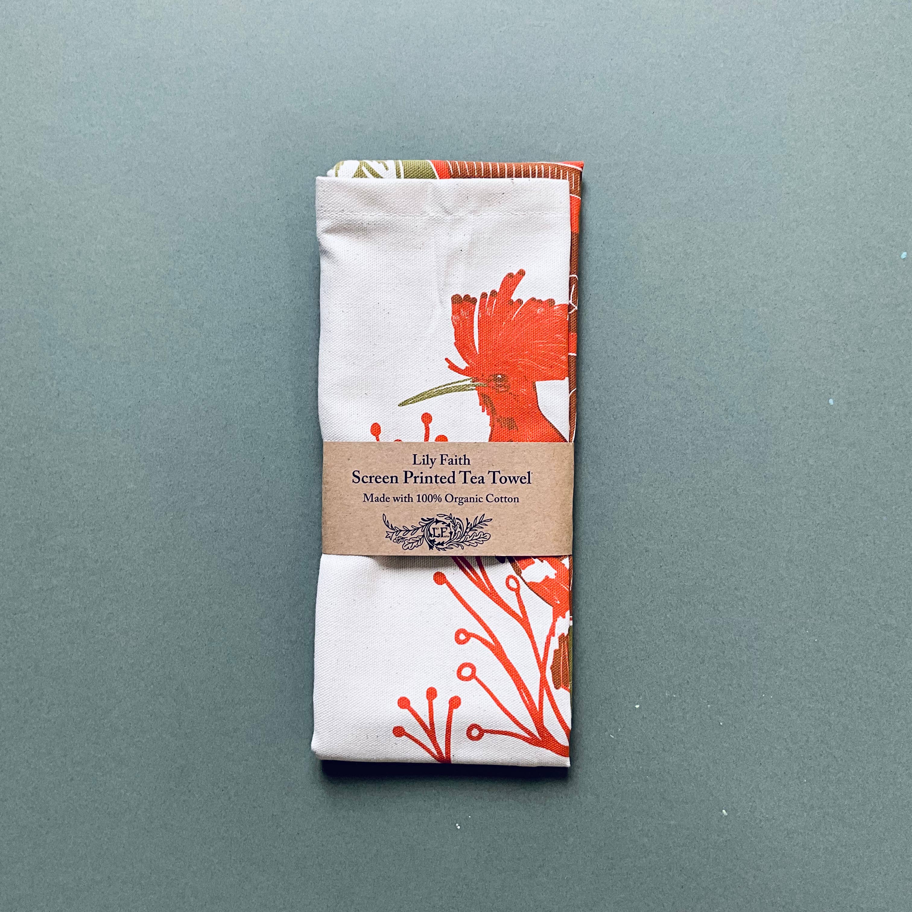 Screen printed tea towel with floral design and brown label on a gray background