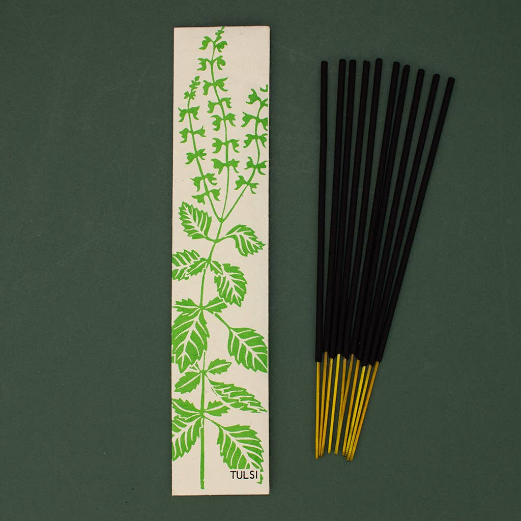 Tulsi incense sticks with a green leaf design on a beige strip against a dark green background