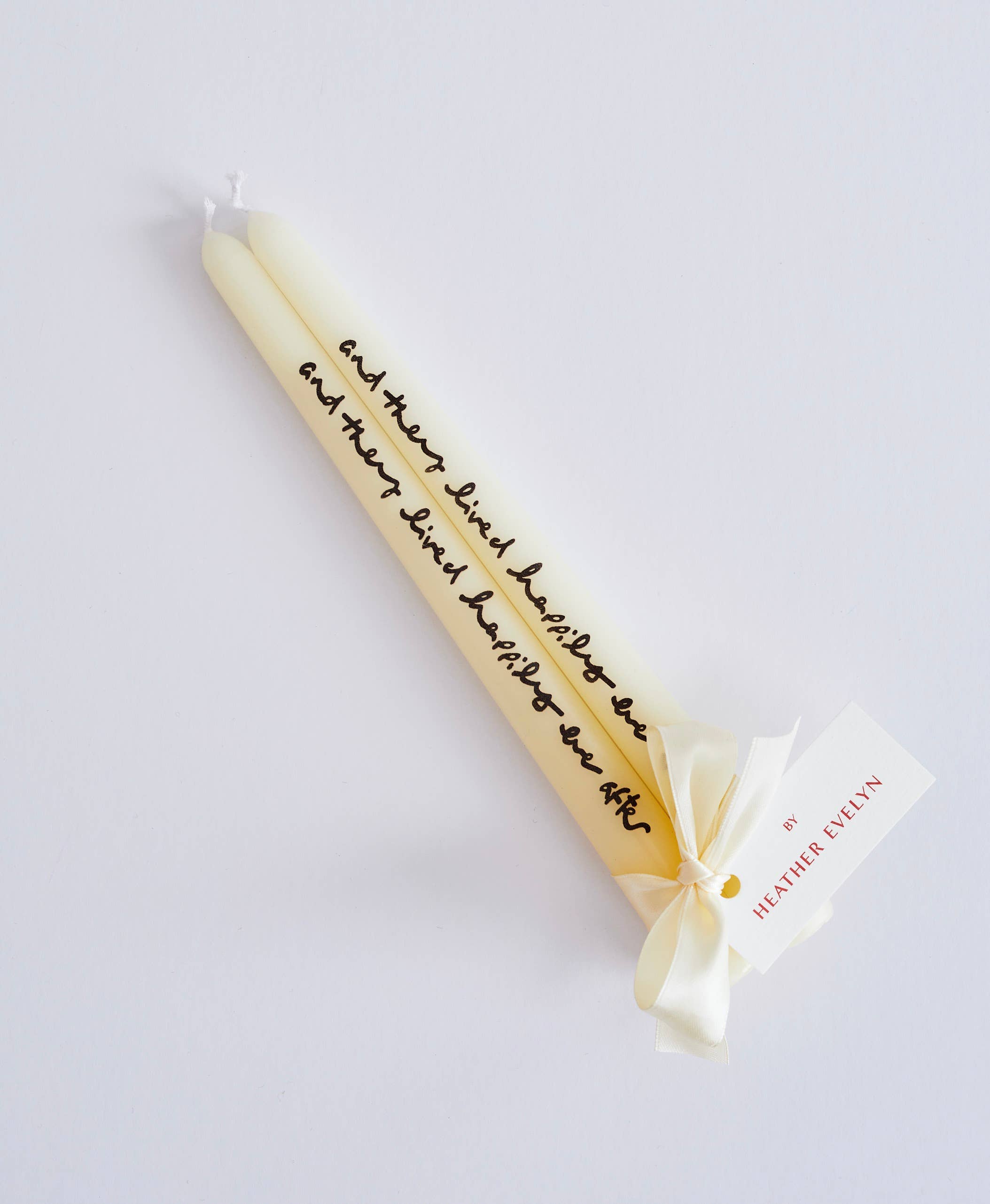 Tall cream candle with text and a bow on a light grey background