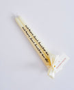 Tall cream candle with text and a bow on a light grey background