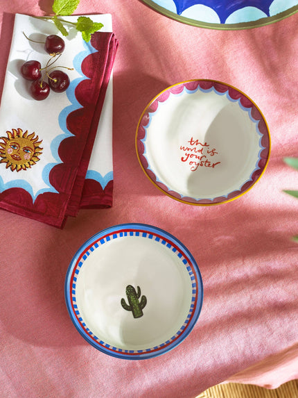 Decorative ceramic bowls with cactus and sun designs on a pink surface.