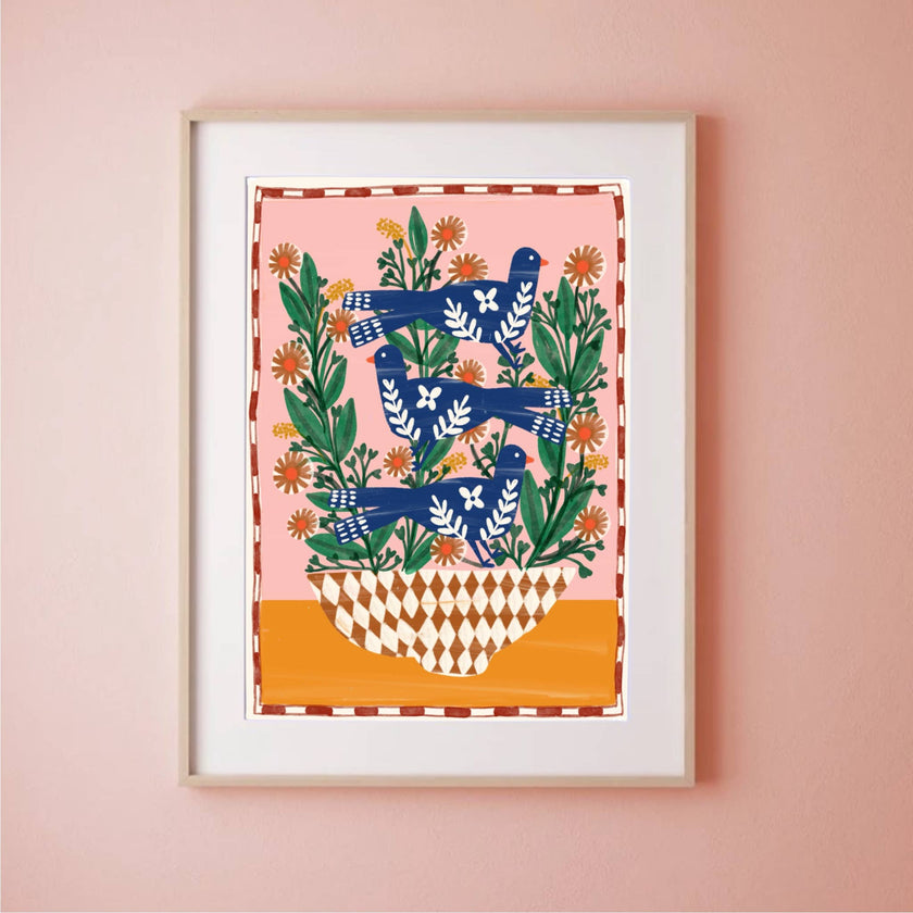 Framed artwork with blue birds and green leaves on a pink wall