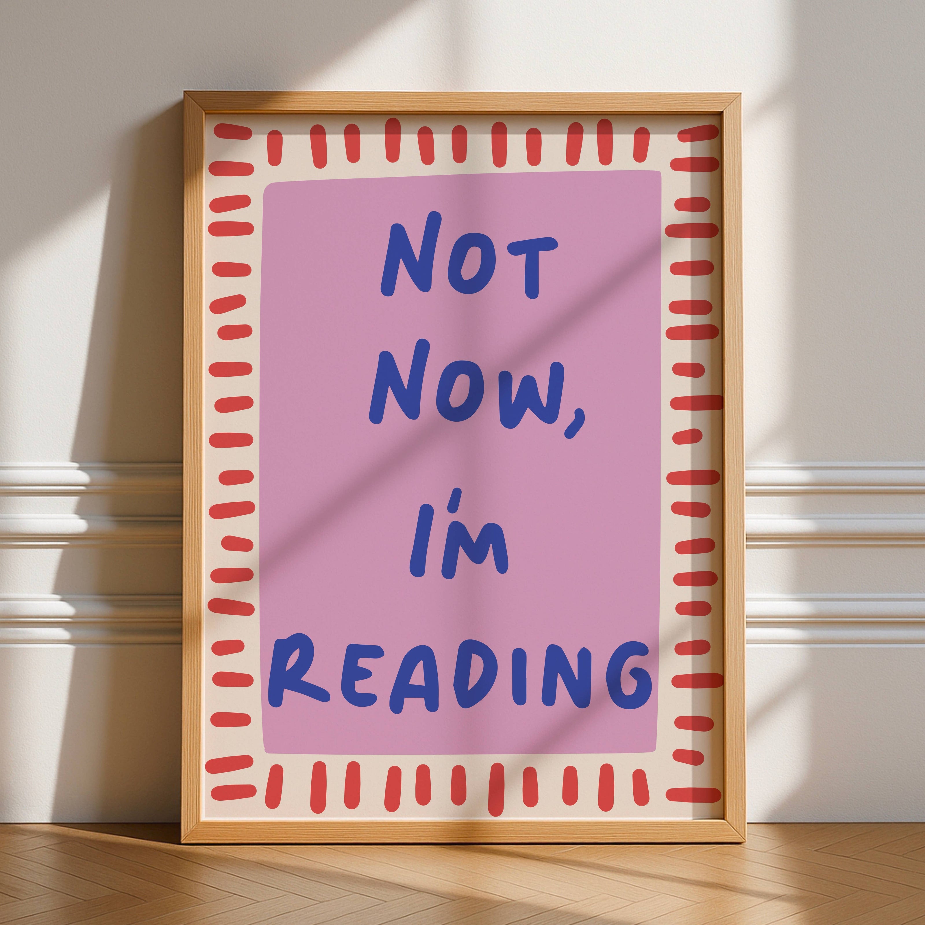 Framed poster with 'Not Now, I'm Reading' text on a pink background