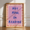 Framed poster with 'Not Now, I'm Reading' text on a pink background