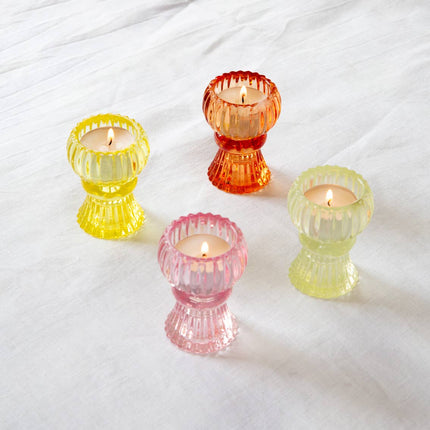 Four colorful glass candle holders with candles on a white fabric background