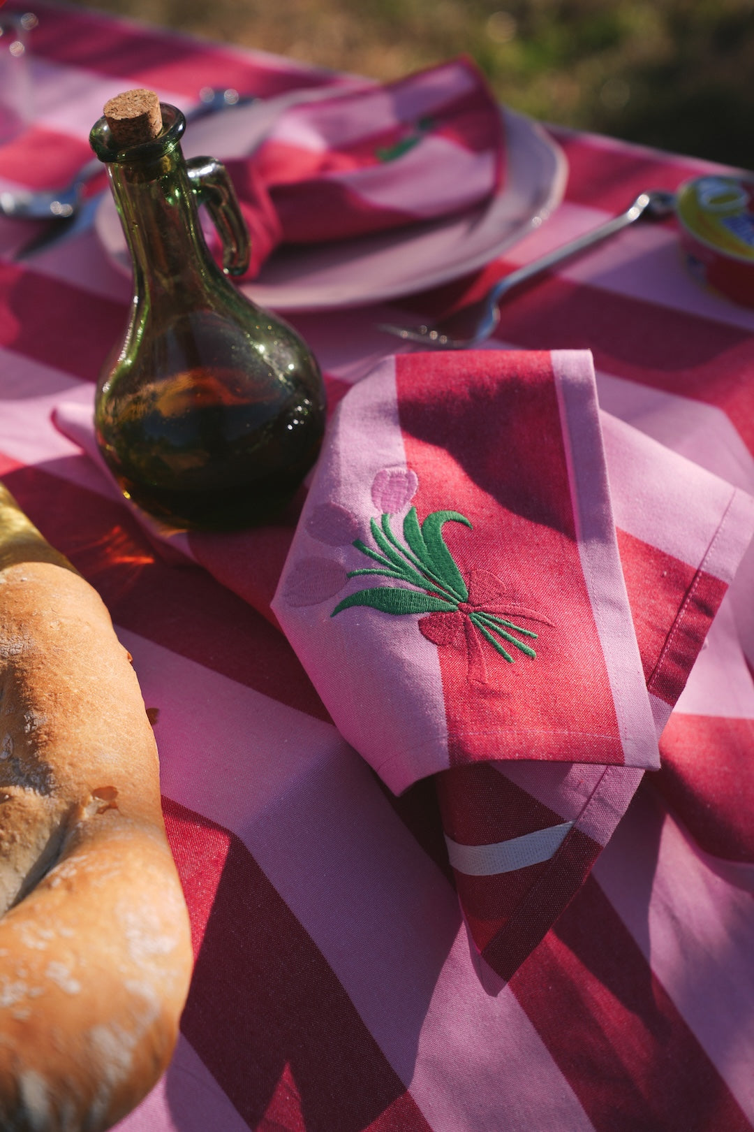 Red and pink striped tablecloth with embroidered tulips on napkin on a table setting outdoors.