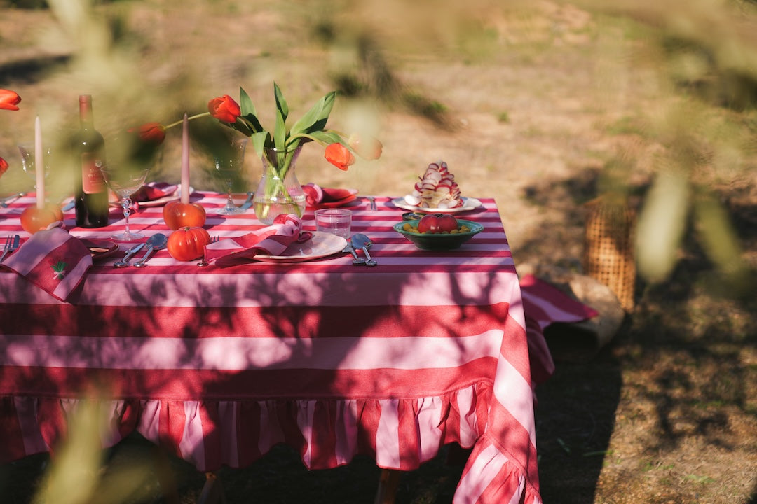Outdoor table setting with a red and white checkered tablecloth, flowers, and cutlery.