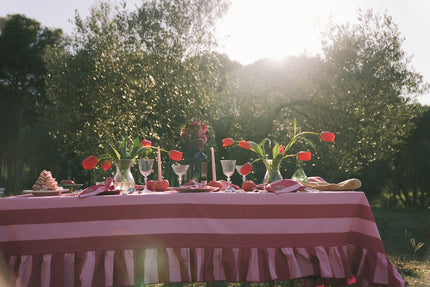 Dining table set with flowers, glasses, and candles outdoors with a pink and white striped tablecloth.