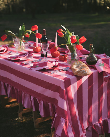 Decorated outdoor table with red and white striped tablecloth, flowers, and cutlery.