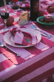 Table setting with a red and pink striped tablecloth, wine glasses, and a plate with a red and pink decorative napkin.