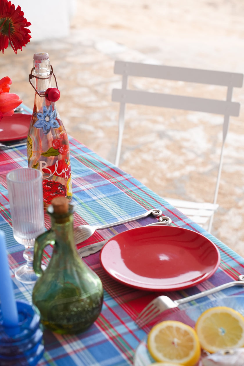 Table setting with plaid tablecloth, bread, and wine glasses outdoors.