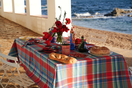 Dining table set for two with a red and blue bright check tablecloth by the beach.