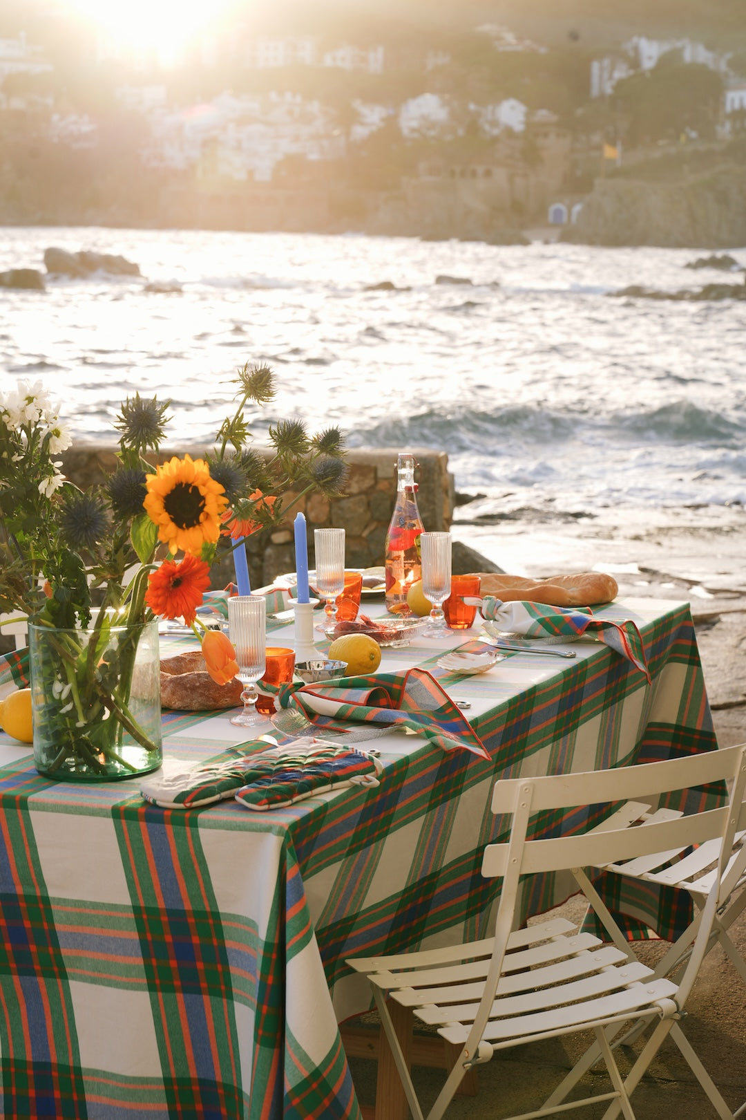 Dining table with flowers , lemons and candles with a check tablecloth in green, blue and orange by the sea.