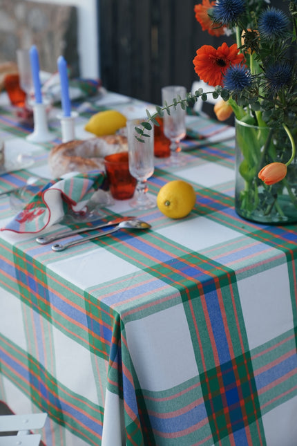 Dining table with flowers , lemons and candles with a check tablecloth in green, blue and orange.