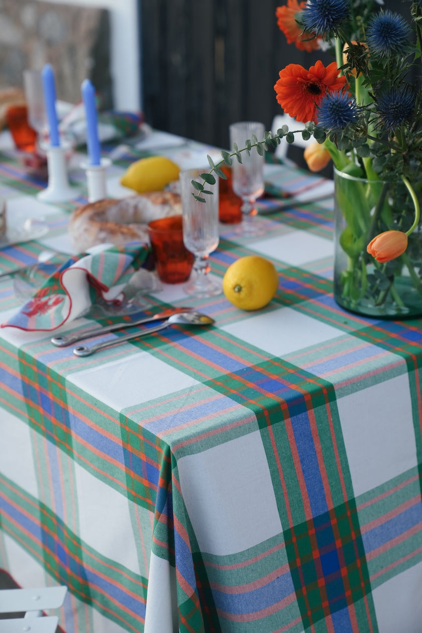 Dining table with flowers , lemons and candles with a check tablecloth in green, blue and orange.