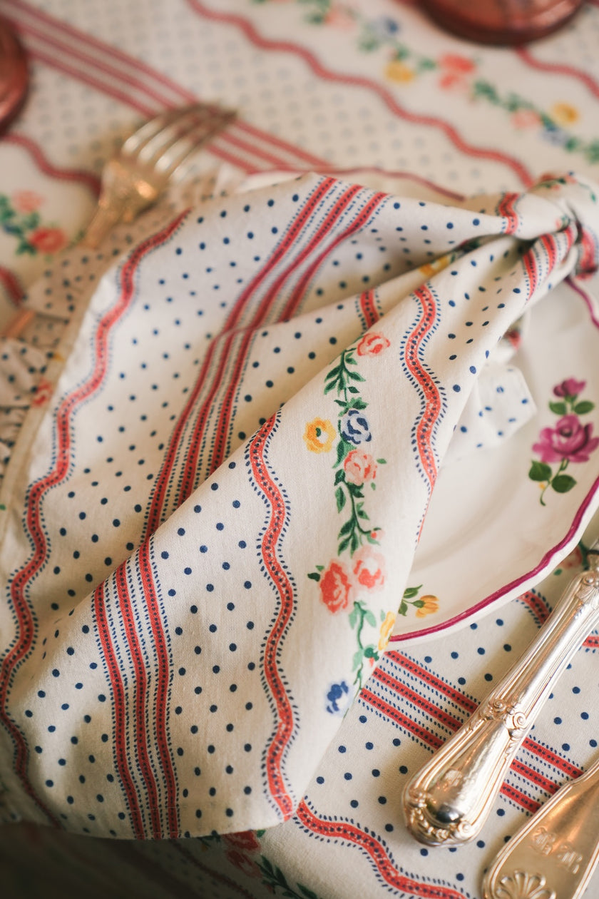 Decorative napkin with floral and polka dot patterns on a tablecloth with floral designs.