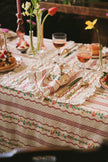 Decorative table setting with floral tablecloth, placemat, napkin, cutlery, and glasses.