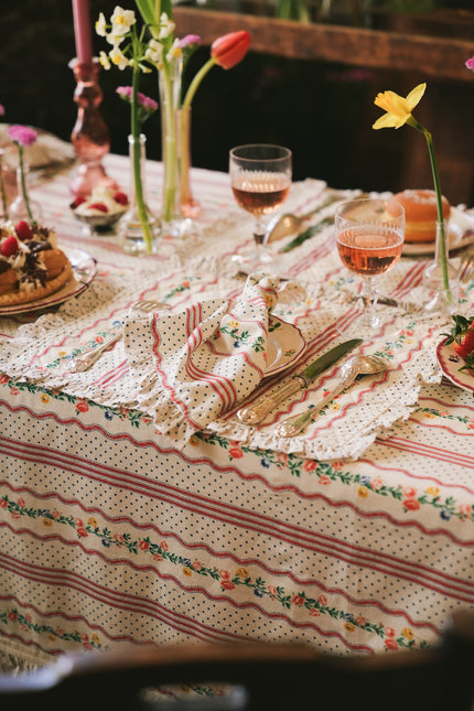 Decorative table setting with floral tablecloth, placemat, napkin, cutlery, and glasses.