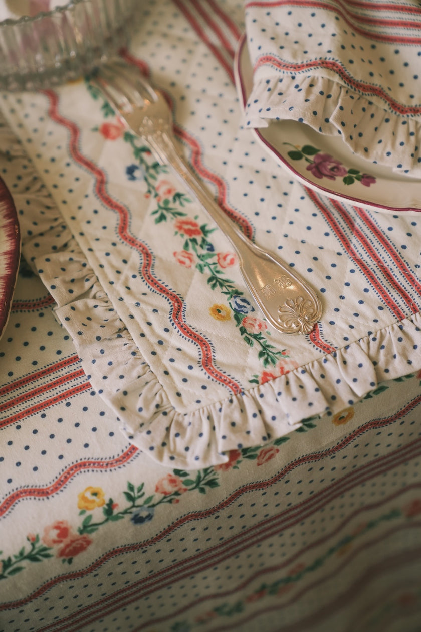 Decorative placemat with ruffle in a floral pattern and a fork on a matching fabric tablecloth