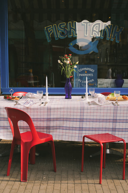 Red chairs and table with a checkered tablecloth in front of a window with 'Fish Tank' branding.